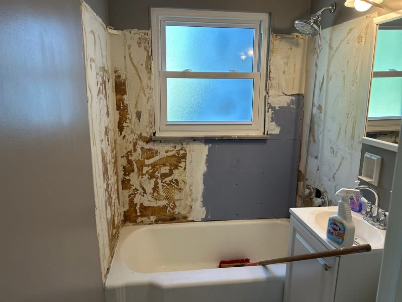 Bathtub and surround before — stripped, patched walls mid-renovation