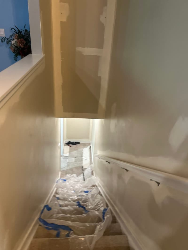Stairwell before — patched drywall and primer, plastic sheeting on stairs